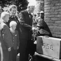 man and woman with two boys, man is placing a cornerstone