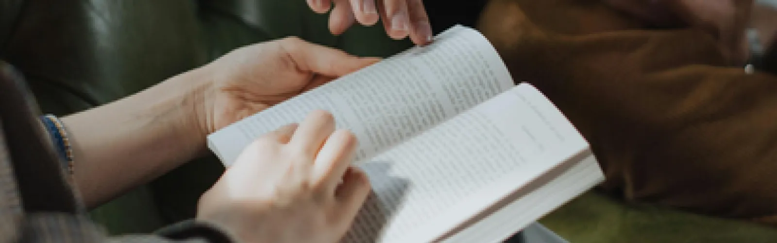 Person holding open book with second person's hand gesturing toward the book